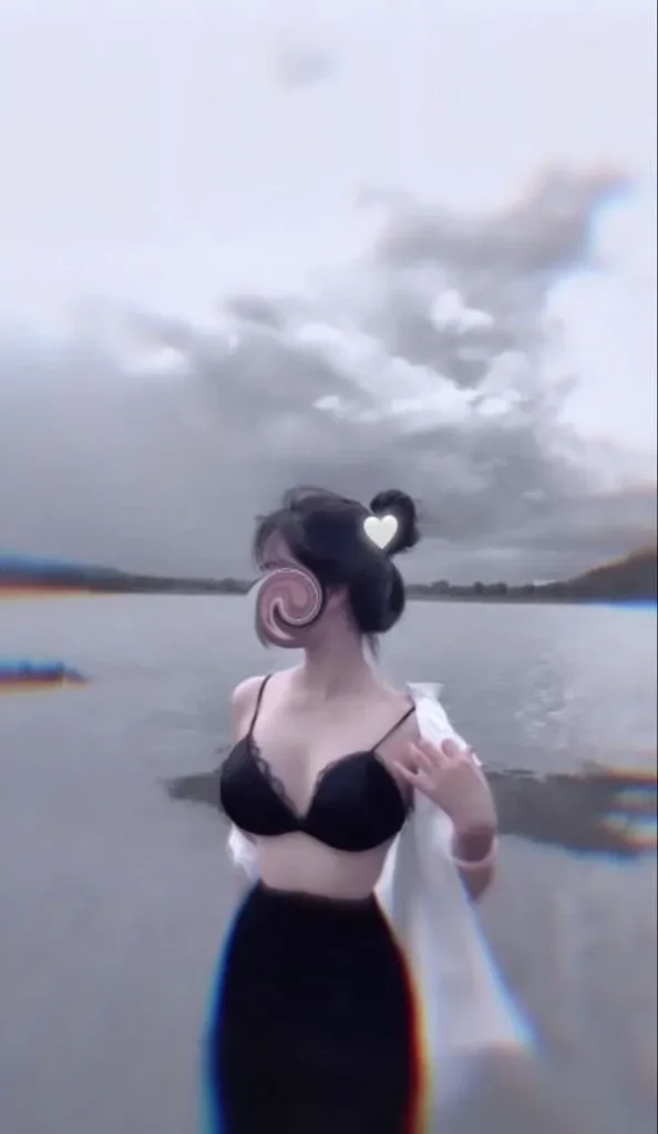 Ảnh gái bikini che mặt đứng bên bãi biển, tay che nắng, tóc búi gọn, da bắt sáng, dáng thon gợi cảm.