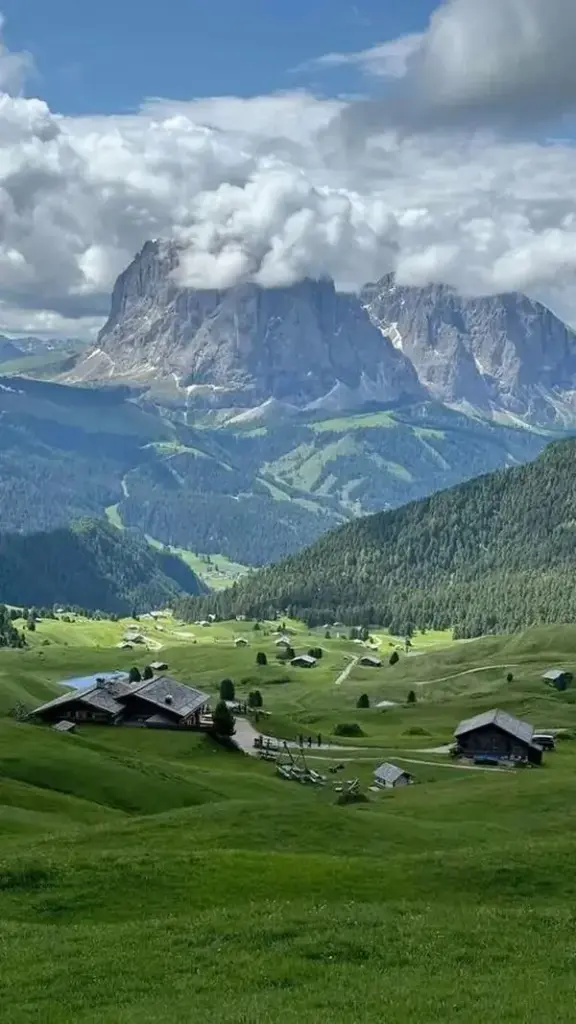 Một thung lũng xanh nằm dưới dãy núi phủ mây xám, các mái nhà nhỏ chấm giữa đồng cỏ khiến tranh cảnh vật màn hình này có vẻ yên ả và sâu