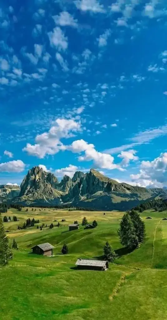 Ảnh bìa điện thoại bãi cỏ xanh mở ra dưới bầu trời xanh đầy mây trắng, dãy núi xa và ghế gỗ nhỏ khiến khung hình đồng quê vừa mát vừa dễ nhìn